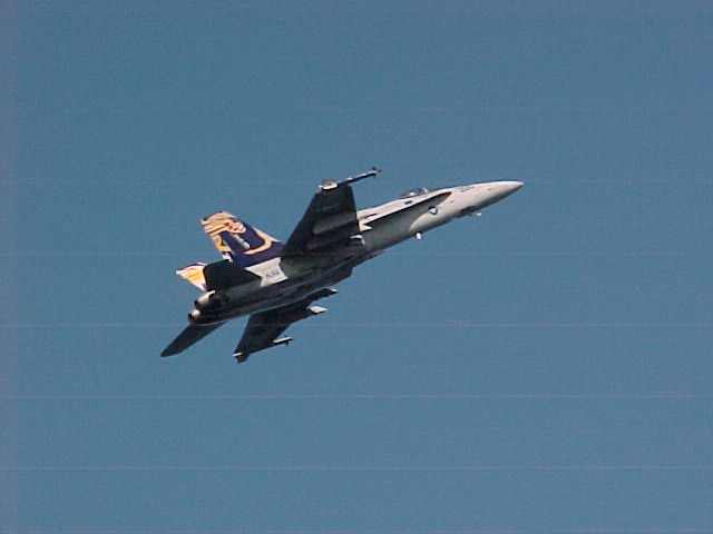 an f18 hornet flys above the uss kitty hawk aircraft carrier
